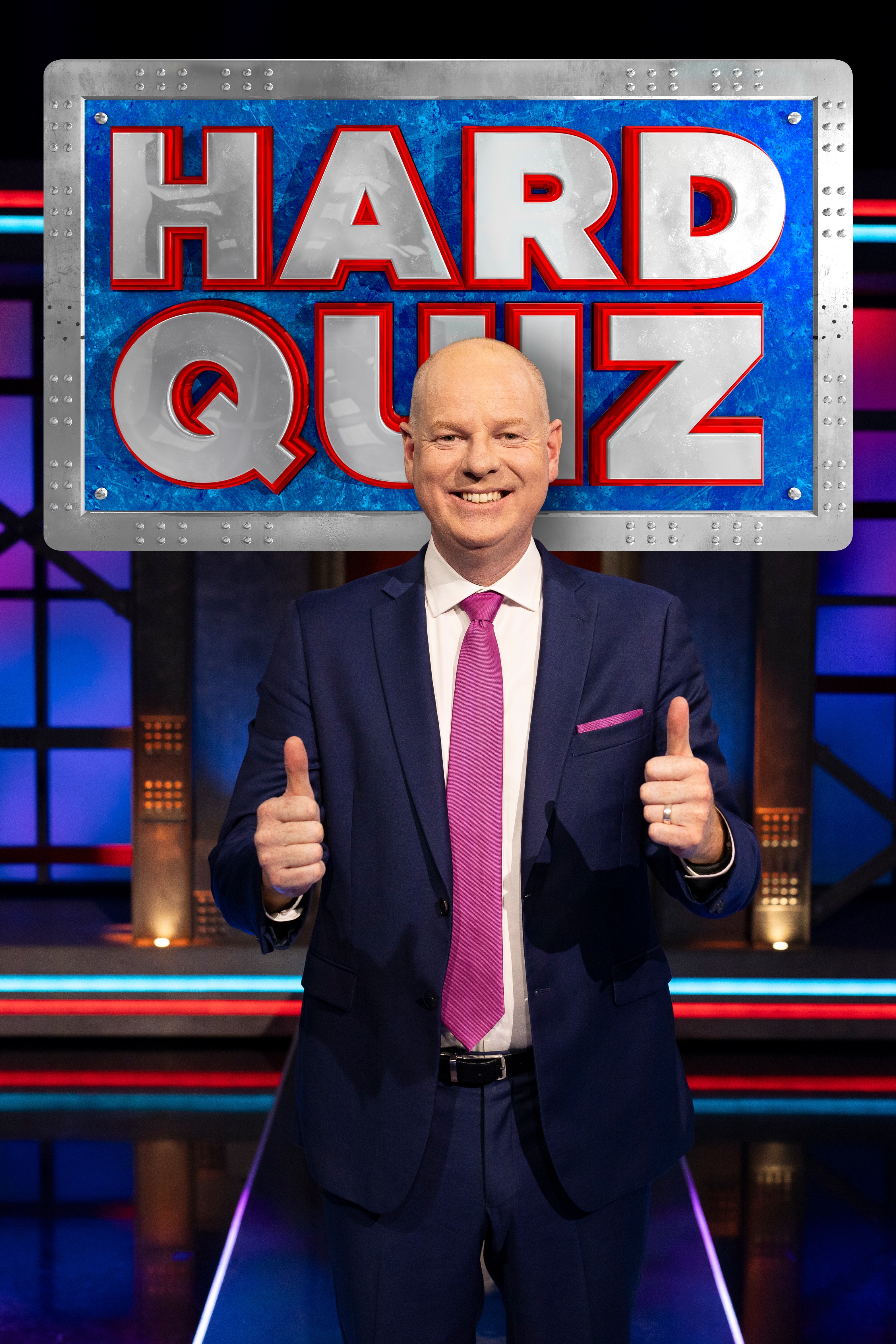 Tom Gleeson smiling with two thumbs up in front of the Hard Quiz logo.