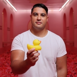 Marc Fennell stands in pink room, holding a yellow rubber duck.
