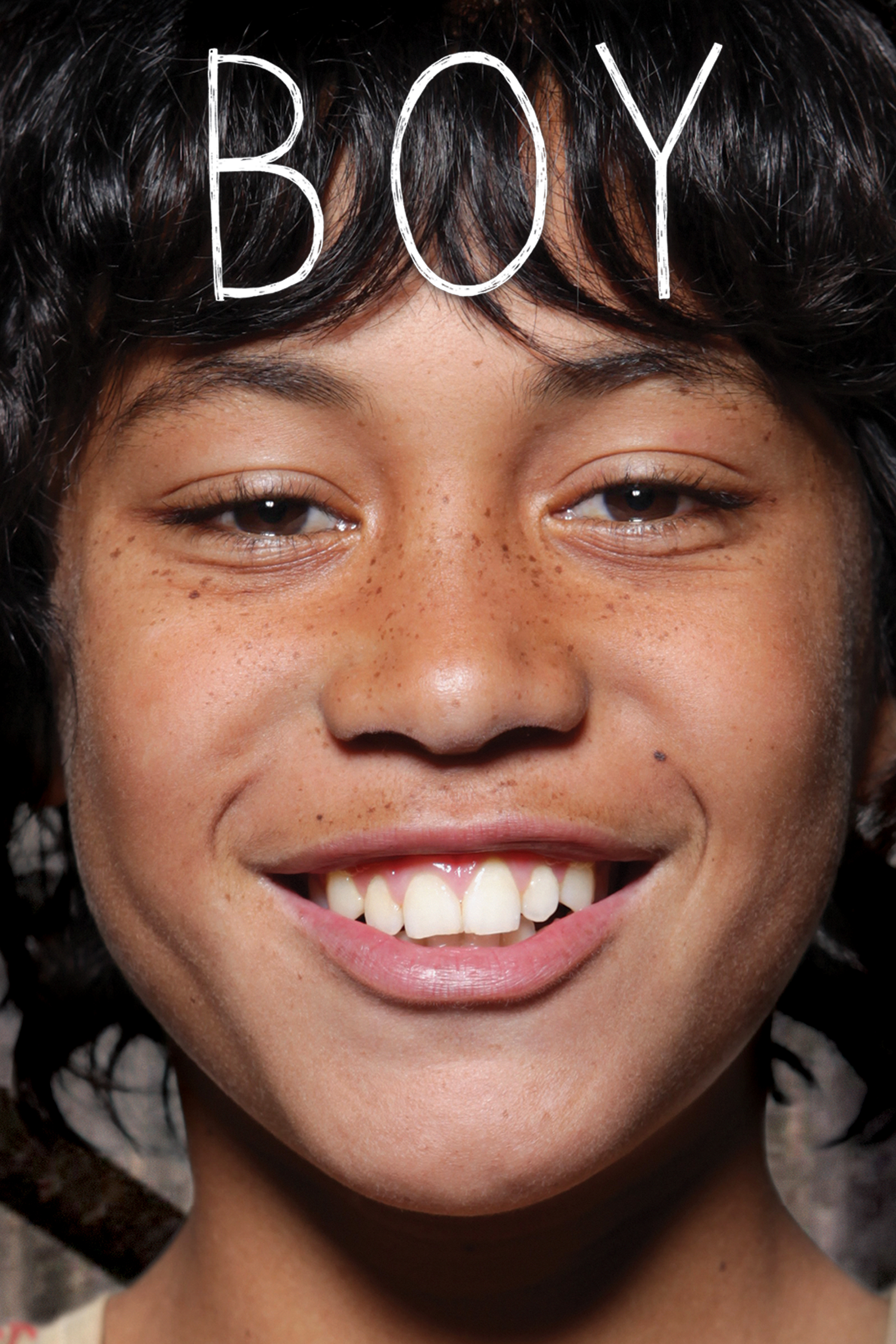 Close-up portrait of a young Māori boy smiling broadly, with the word BOY in large white letters at the top of the image.