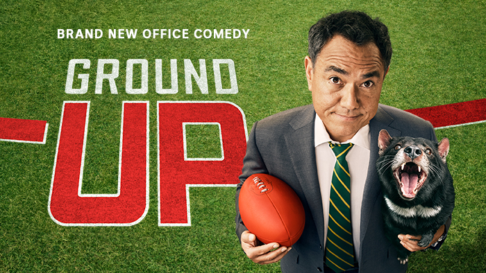 can I have alt text for this?4:30 PMClaude responded: Promotional image for Ground Up, a brand new office comedy.Promotional image for Ground Up, a brand new office comedy. A man in a suit and striped tie holds a football and a Tasmanian devil against a football oval background.