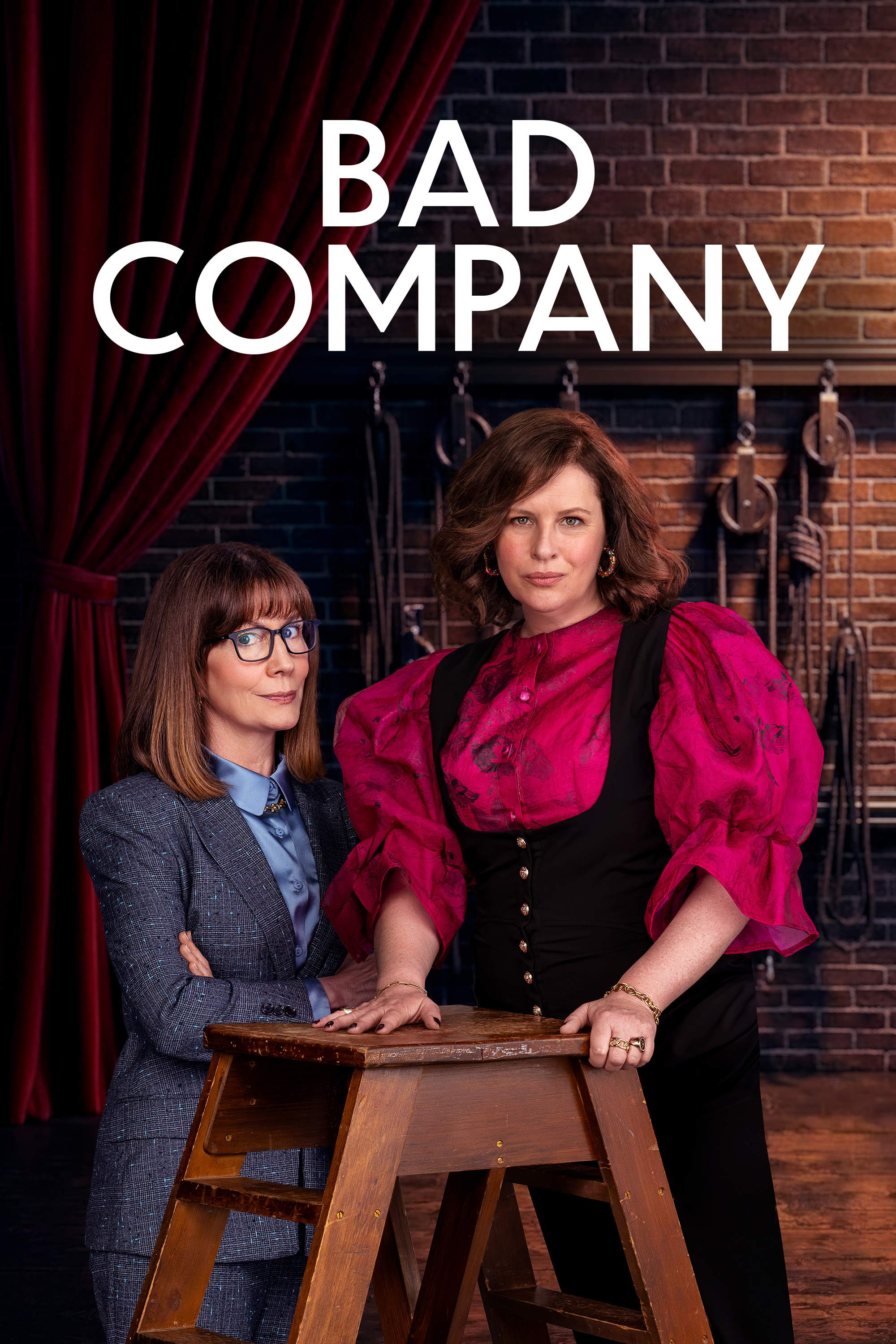 Anne Edmonds and Kitty Flanagan stand in a dramatic pose against a dark red backdrop with the show title Bad Company above them.