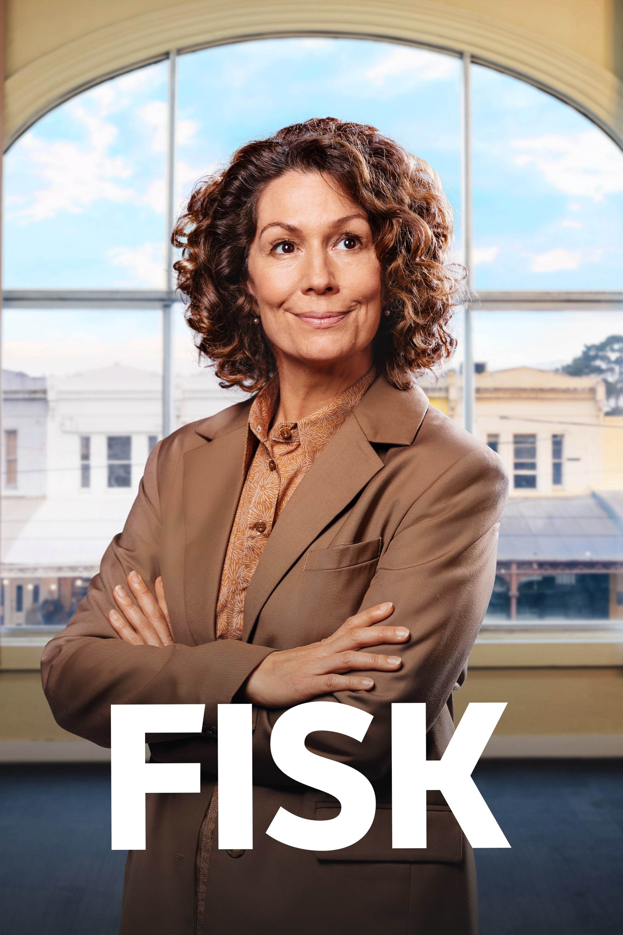 Kitty Flanagan stands with arms crossed in front of a large window, with the show title Fisk below her.