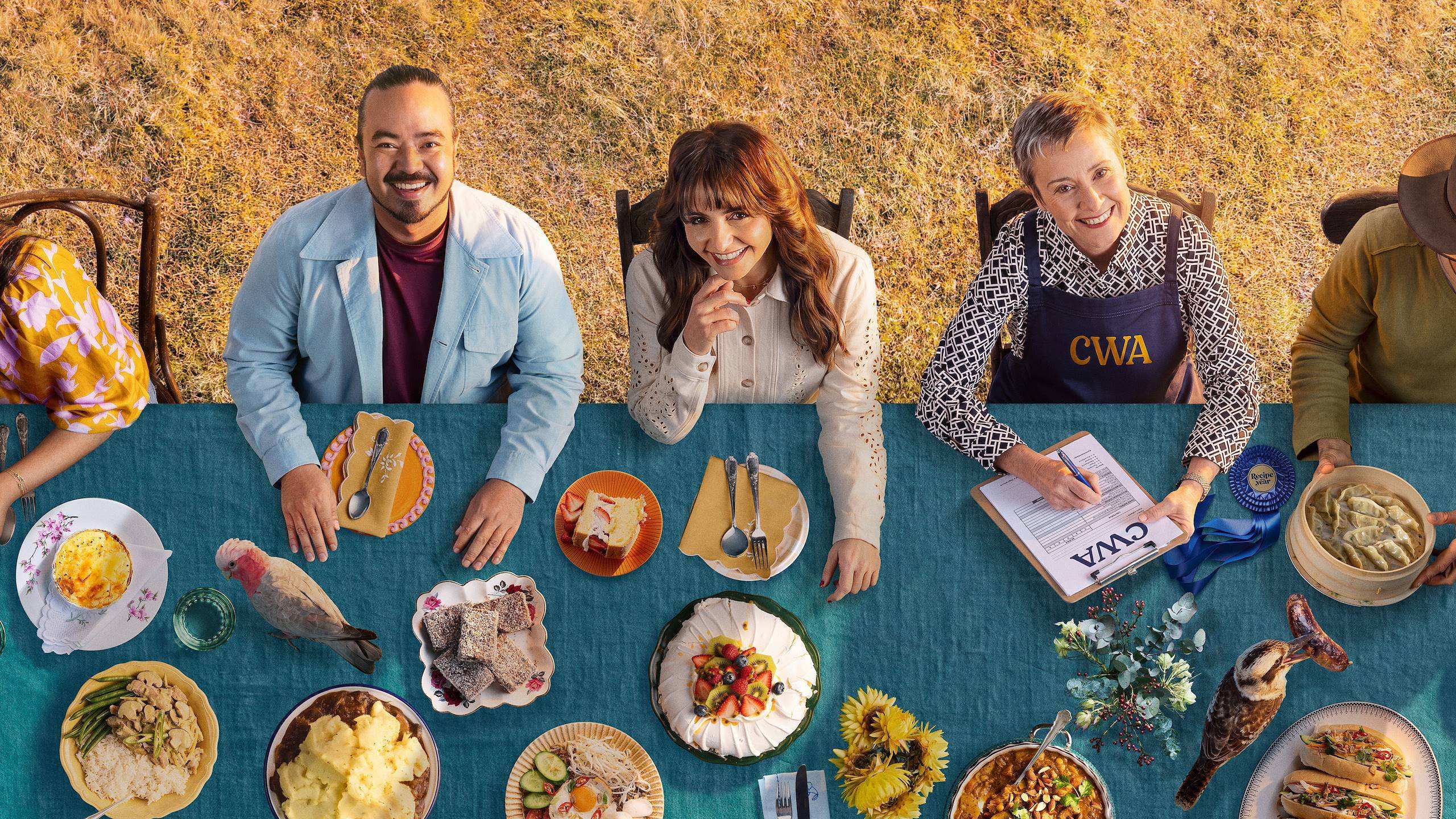 Promotional poster for Recipe of the Year, showing judges Adam Liaw and Pia Miranda alongside a Country Women's Association representative seated at an outdoor table filled with home cooked dishes.